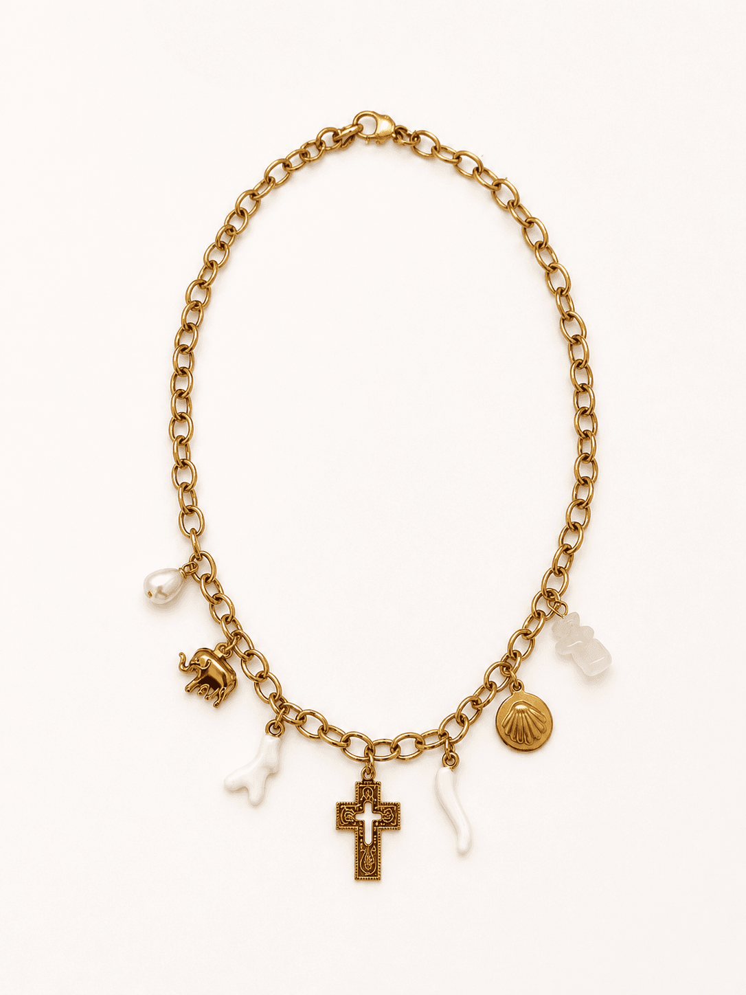 Collier Marina à plat sur fond blanc, chaîne forçat d'or et 6 pendentifs visibles — éléphant d'or, corail blanc, perle baroque, crucifix byzantin ciselé, coquille pèlerine et corail blanc