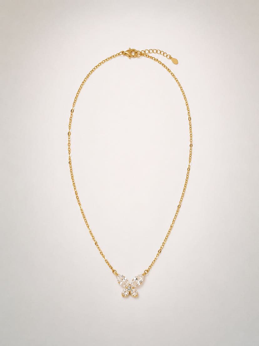 Collier Psyché à plat sur fond crème pâle, chaîne fine à maillons forçat alternés et pendentif papillon centré en bas — quatre topazes blanches taille marquise composant les ailes et une perle ronde centrale