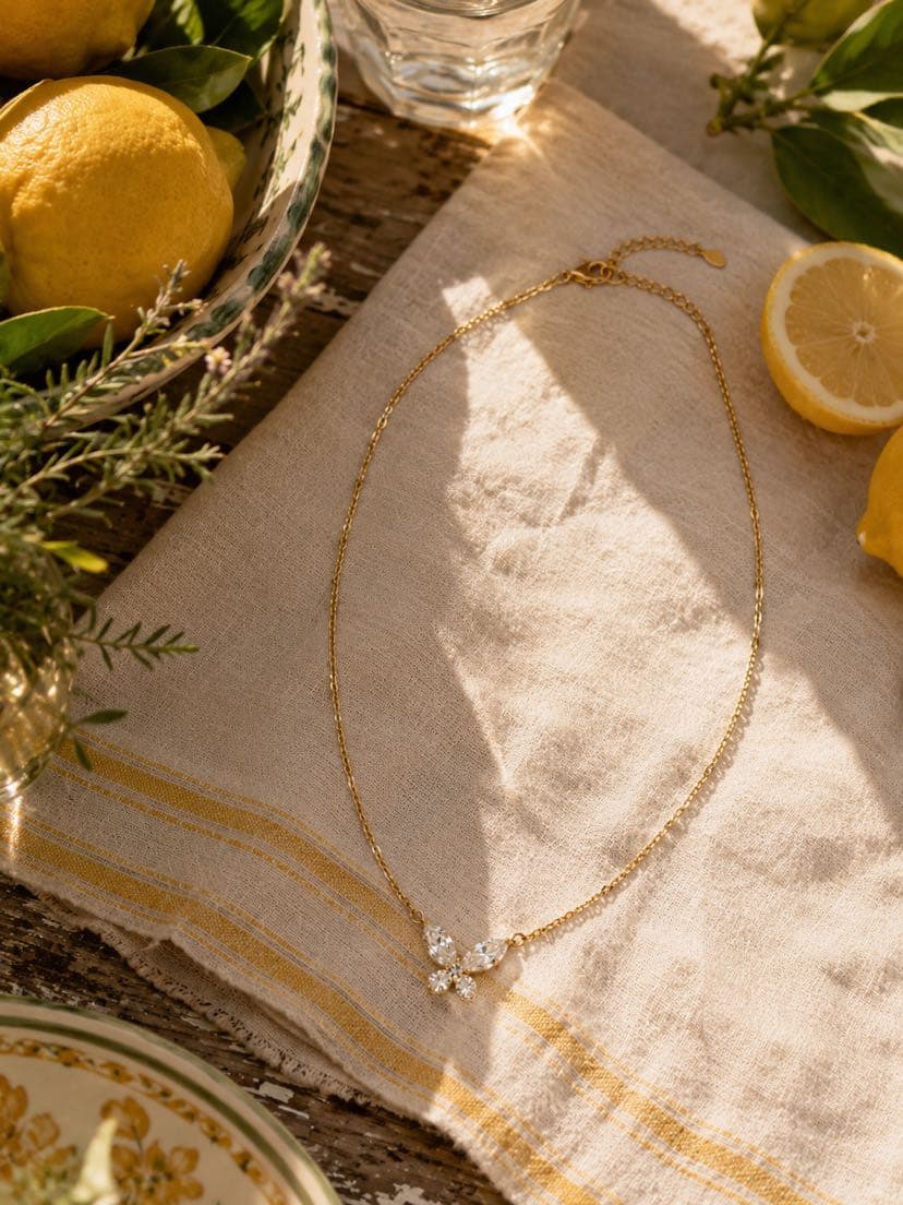 Collier Psyché posé sur un torchon de lin écru rayé de jaune, citrons entiers et tranchés dans une coupe en céramique vintage, brins de romarin, ombre dansante du midi
