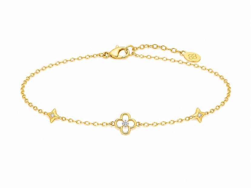 Bracelet Cicadu à plat fond blanc, chaîne or jaune en ovale, trèfle 4 pétales ajouré au centre avec zircon, deux étoiles à 4 branches latérales, fermoir mousqueton et plaque signature fleur à droite