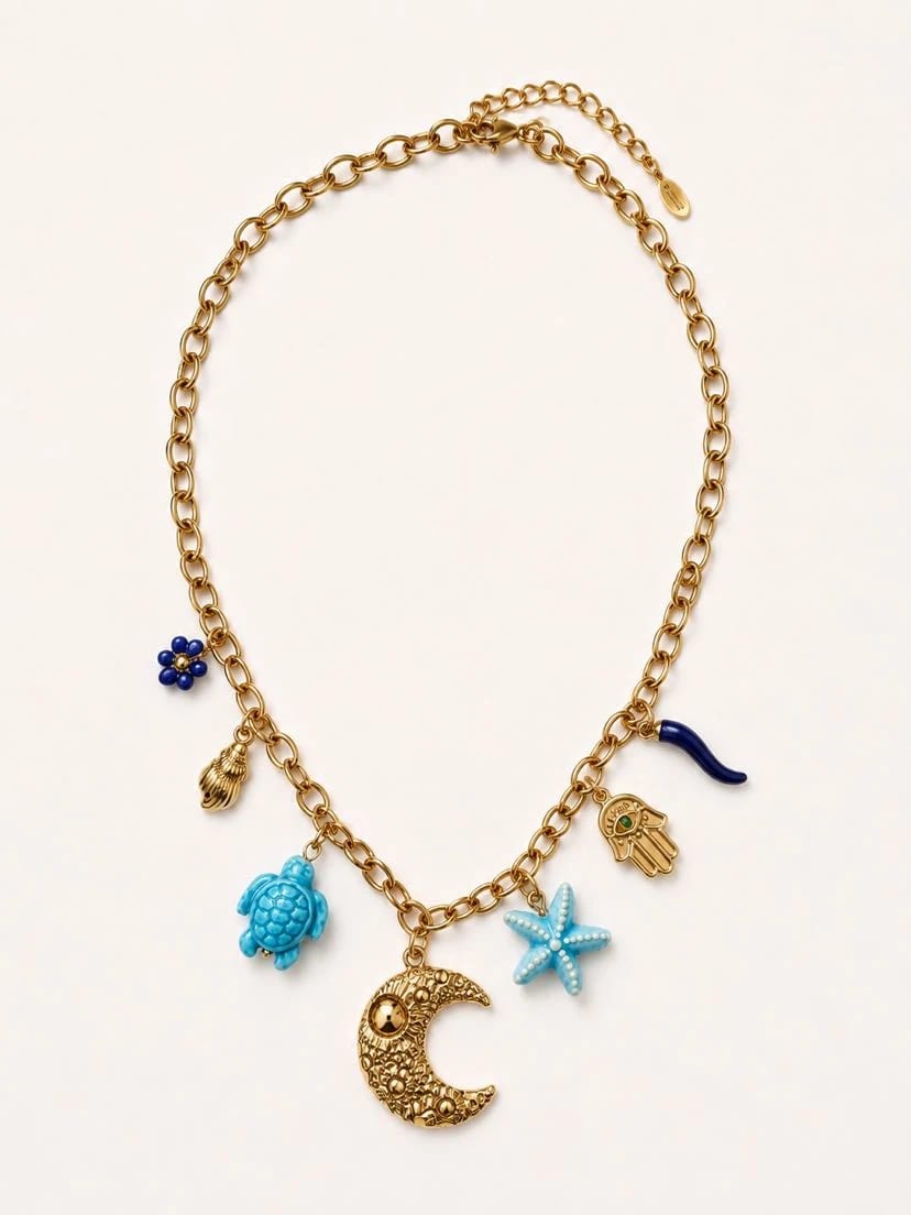 Collier Azulina à plat sur fond crème, chaîne forçat d'or et 7 breloques en cluster — fleur de lapis bleu, coquille dorée, tortue turquoise, croissant de lune doré ciselé, étoile de mer turquoise, main de Fatma émaillée, cornicello bleu vitrifié, fermoir et rallonge visibles en haut
