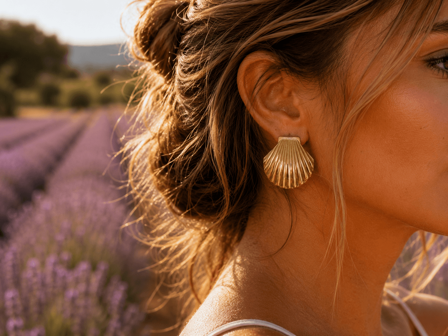 Gros plan macro sur une oreille portant la boucle Vénus, champ de lavande en arrière-plan, lumière dorée du couchant en Provence